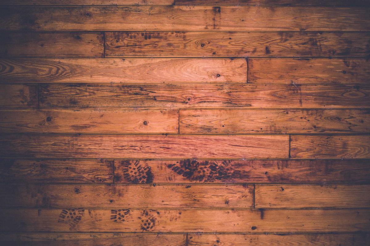 Horizontal wooden floorboards with visible knots, grain patterns, and muddy boot prints across the surface.